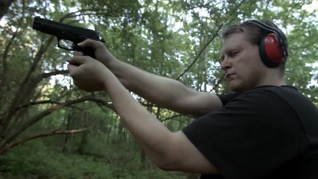 Low, frontal viewpoint of man firing a .44 caliber pistol in woodland.  Muzzle flashes visible.  Recorded in 4K, Ultra High Definition.