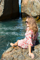 Young woman sitting on rocky seashore.