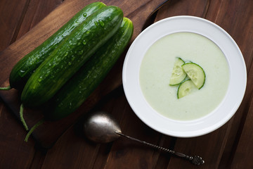 Plate with cucumber cream-soup and fresh cucumbers, top view