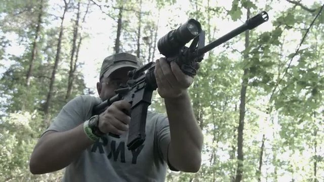Frontal view of man firing an AR-15 assault rifle in woodland setting.  Originally recorded in 4K, Ultra High Definition.