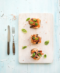 Bruschettas with Prosciutto, roasted melon, soft cheese and basil on wooden serving board over light blue background