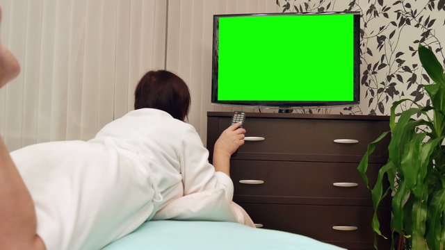 Woman watching TV with green screen. Dolly shot.
