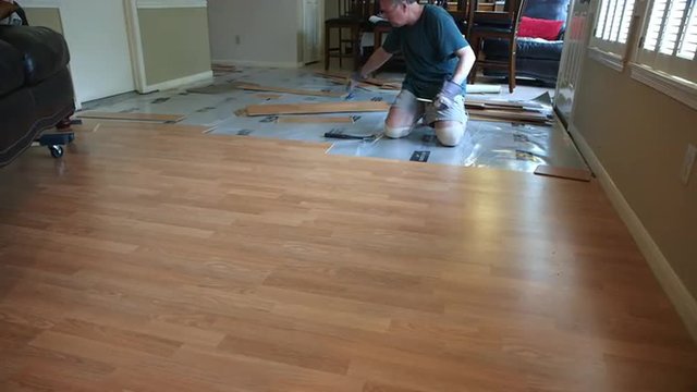 A workman or homeowner handyman type engaged in a DIY project of removing old laminate flooring to prepare for new floor covering.