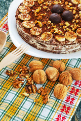 Chocolate cake with nuts and bananas on a plate and walnuts on a yellow napkin