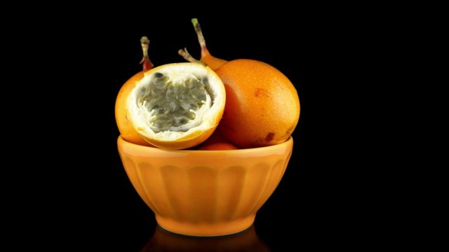 Passion fruit maracuja granadilla on ceramic yellow bowl, black background.