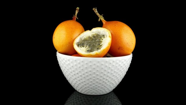 Passion fruit maracuja granadilla on ceramic white bowl, black background.