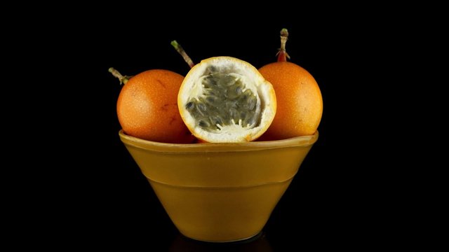 Passion fruit maracuja granadilla on ceramic yellow bowl, black background.
