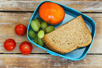 Healthy school lunch box containing brown sandwich with cheese, cherry tomatoes, mandarine and grapes
