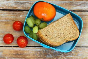 Healthy school lunch box containing brown sandwich with cheese, cherry tomatoes, mandarine and grapes   © graletta
