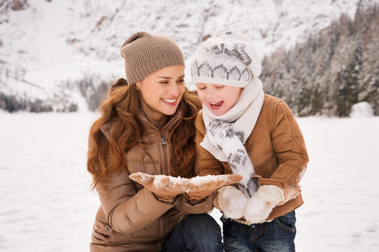 Happy mother and child playing with the snow in winter outdoors
