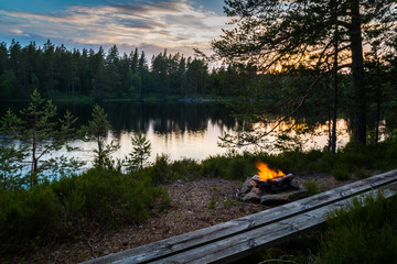 Empty bench at the camp fire in the Swedish forrest, view over the lake.