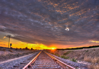 Fototapeta na wymiar Sunset rays streak from below the cirrocumulus clouds over train tracks.