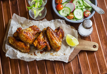 Spicy chicken wings and fresh vegetable salad on wooden background