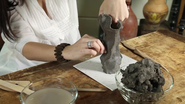 Close-up of hands of a sculptor woman making a sculpture from raw clay
