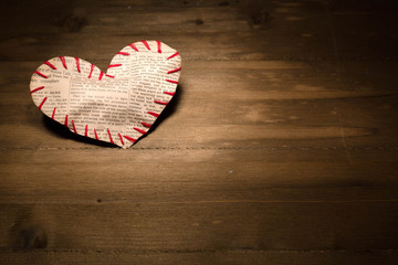 The heart sewed from a newspaper slice by red threads lies on th