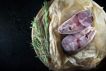 Obraz premium Fillet of raw fish and ingredients for cooking on a dark background in a rustic style. View from above
