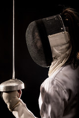 Portrait of woman wearing white fencing costume practicing with the sword. Isolated on black...