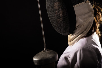 Portrait of woman wearing white fencing costume practicing with the sword. Isolated on black background.
