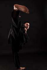 Studio portrait of young karate fighter kicking over black background.