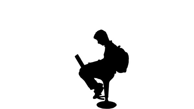 Silhouette of student writing on laptop - 1080p. Silhouette of a sit down student working on his laptop. Full HD