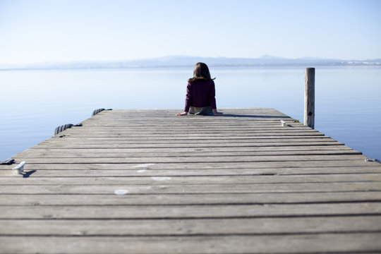 Ni&ntilde;a solitaria sentada en muelle de madera