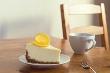 Slice of Lemon Cheesecake on white plate on wooden background, toned image