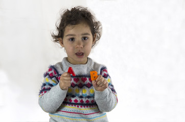 esmer küçük kız çocuğu öğrenci anaokulu kreş eğitimi alıyor, harfler ve şekilleri öğreten siyah tahta tutuyor ve öğretmenin verdiği dersi okuyor