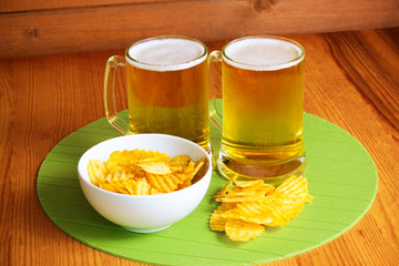 Beer mugs and potato chips on wooden table
