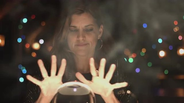 Fortune teller beckons people to join her in viewing a crystal ball.  Medium close up.  UHD 4K.