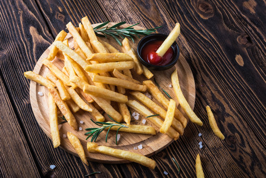 French fries with ketchup and rosemary on wooden background