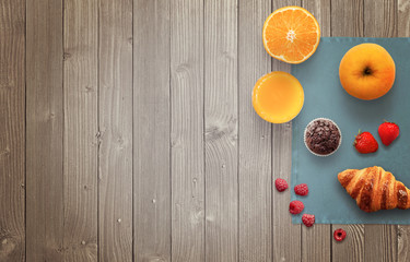 Fruit breakfast with free space for text on wooden table. Jar of jam, strawberry, raspberry, juice, apple, orange, tablecloth, muffin, croissant, wooden table with top view.