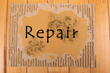Word Repair on piece of cardboard on wooden background