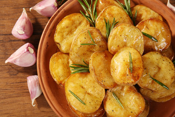 Delicious baked potato with rosemary in bowl on table close up