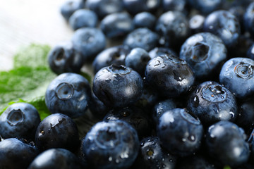 Tasty ripe blueberries with green leaves close up