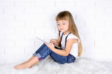 Little girl with tablet on brick wall background