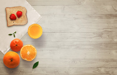 Fruit breakfast with free space for text on wooden table. Jar of jam, strawberry, juice, orange, tablecloth, toast, wooden table with top view.