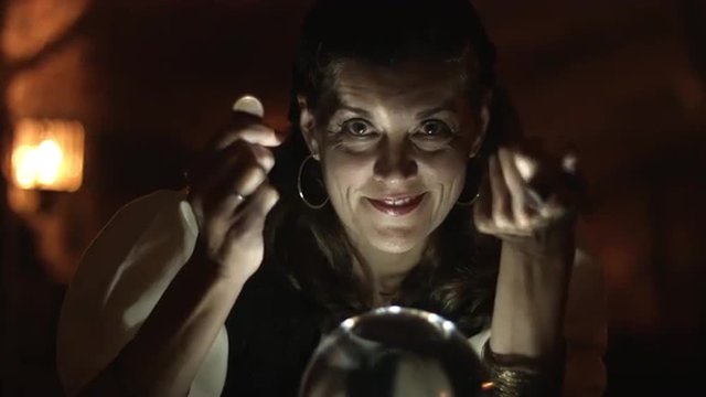 Fortune teller holds a coin and beckons people to her crystal ball.  Close up.  UHD 4K.