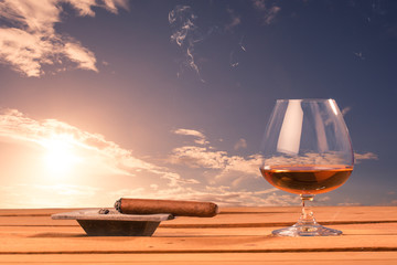 Cognac Glass und Zigarre vor Sonnenuntergang auf Holztisch, Symb