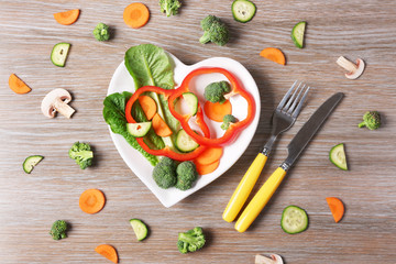 Useful cut vegetables on a plate in the form of heart on wooden table top view