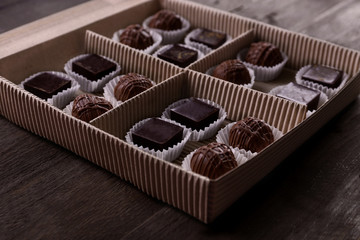 Delicious chocolate candies in paper box on wooden background, close up