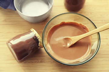 Melted chocolate on glass bowl on tray, on wooden background