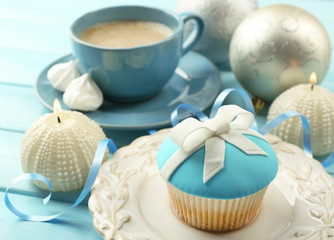 Tasty cupcake with bow, coffee cup and Christmas toys on color wooden background