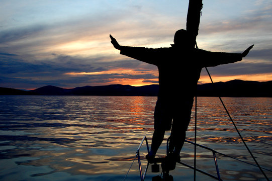 Silhouette of a man standing on the bow of a yacht admiring the sunset