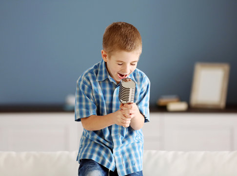 Little boy singing into the microphone on a sofa at home