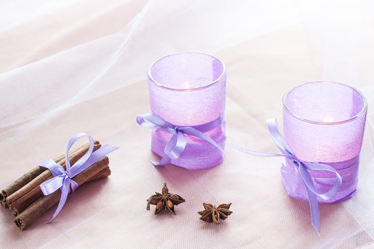 Two aromatic candles in glass candlesticks with lavender paper, cinnamon and anise on table close up