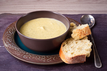 Fresh, home made broccoli and cheddar cheese soup served with a slice of sourdough bread on a stone slate table top.