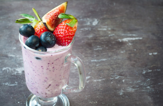 Healthy breakfast smoothie milkshake made from blended blueberries and strawberries with kefir yogurt. Served in a glass topped with fresh fig, blueberries and strawberries isolated on black.