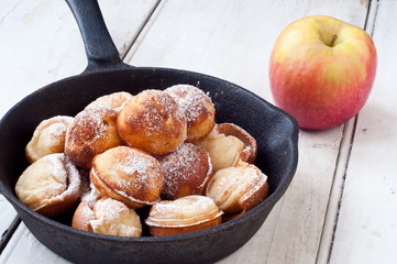 Danish style aebleskiver apple pancakes or pancake puffs served in a cast iron pan on white rustic boards.