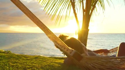 Romantic couple relaxing in tropical hammock at sunset. Summer Luxury Vacation. SLOW MOTION. 