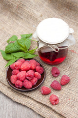 Raspberry preserve in glass jar and fresh raspberries on a plate